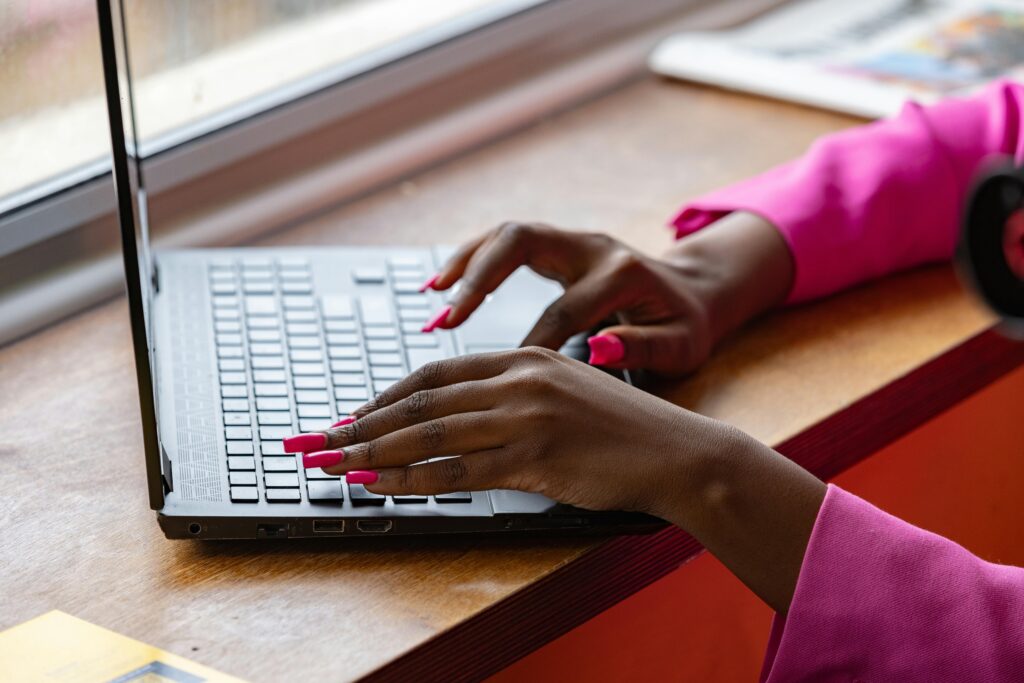 photo of brown feminine hands with long pink square nails and pink long sleeves typing on a computer for the blog post, What Is a Sales Funnel in Digital Marketing? The Ultimate Guide for 2025